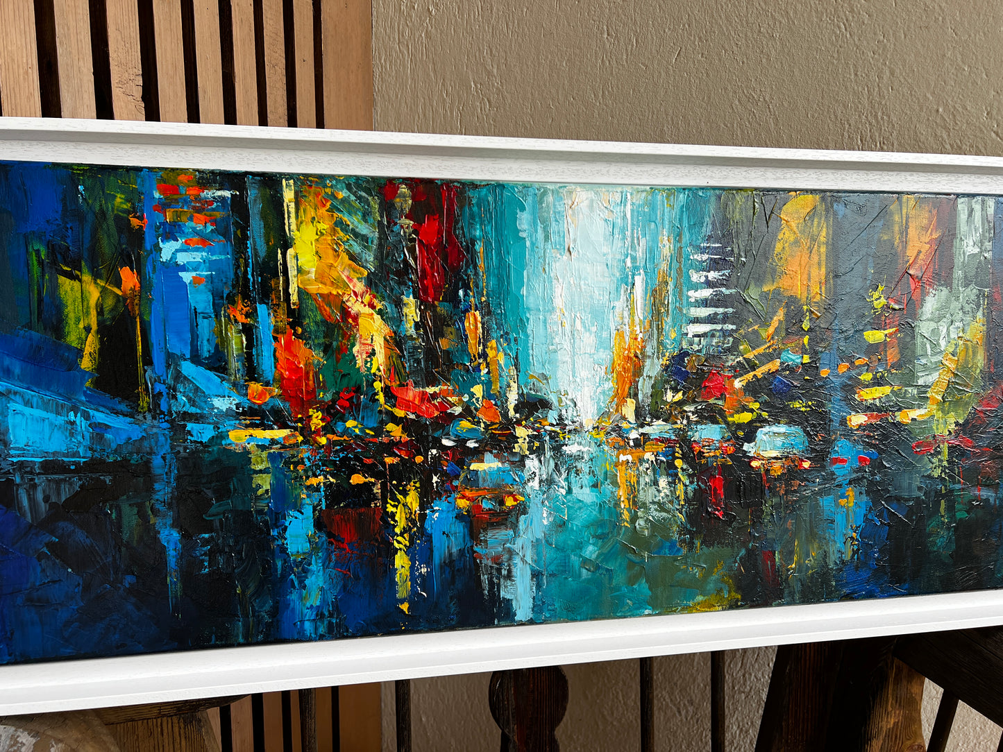 Framed abstract cityscape painting with vibrant colors on a neutral background