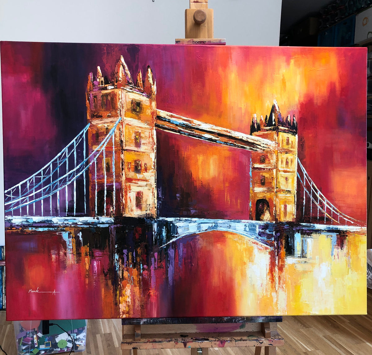 An expressive painting of Tower Bridge in London, rendered in vibrant red, orange, yellow, and dark purple tones, displayed on a wooden easel in an artist's studio.