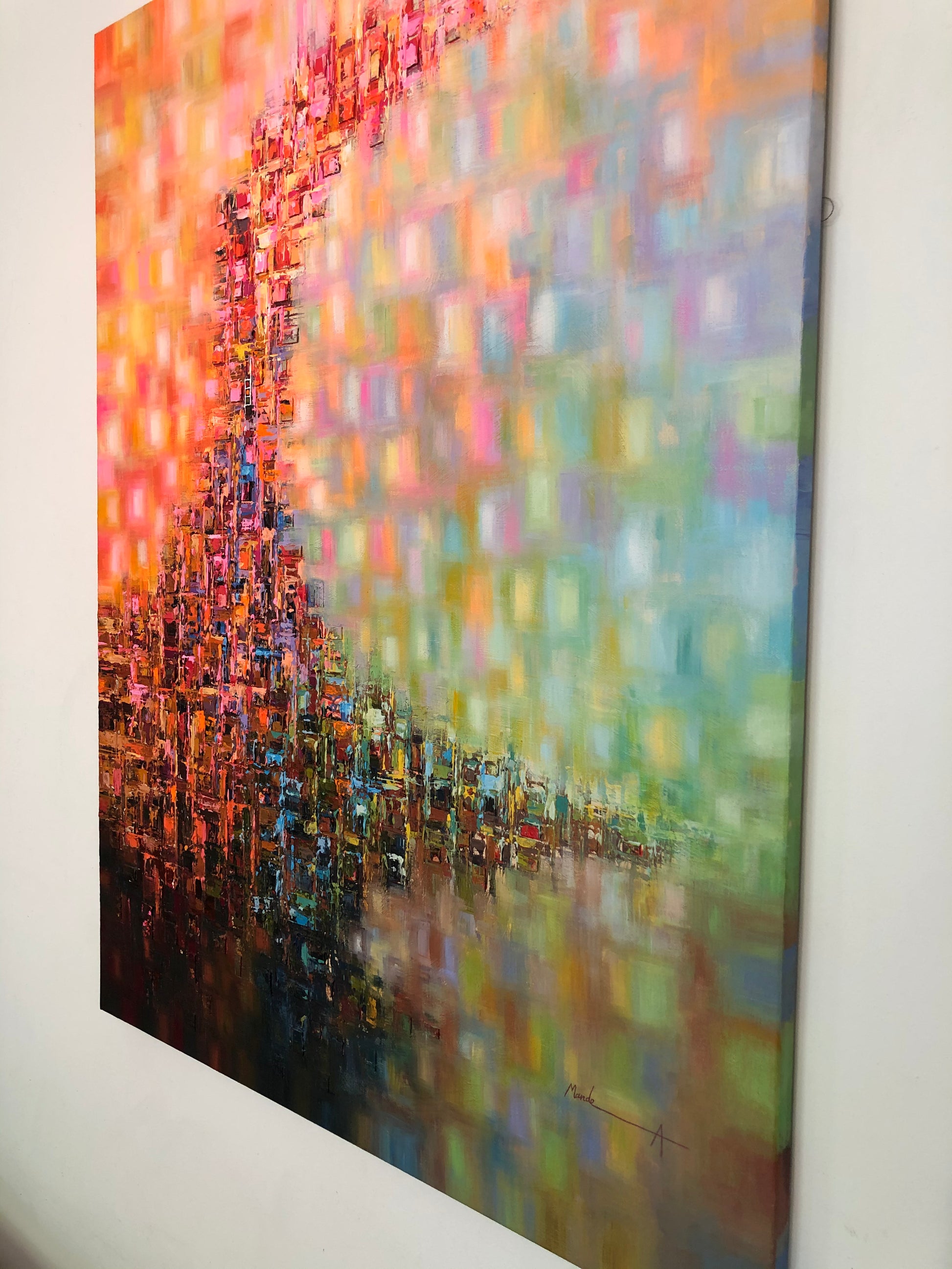 A vertical abstract canvas painting hanging on a white wall, featuring a dense, textured mosaic of orange, red, pink, blue, green, and yellow tones with a darker, painterly lower section.