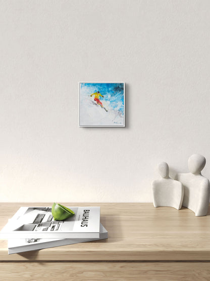 Framed artwork of a skier on a white wall above a wooden surface with magazines and sculptures.